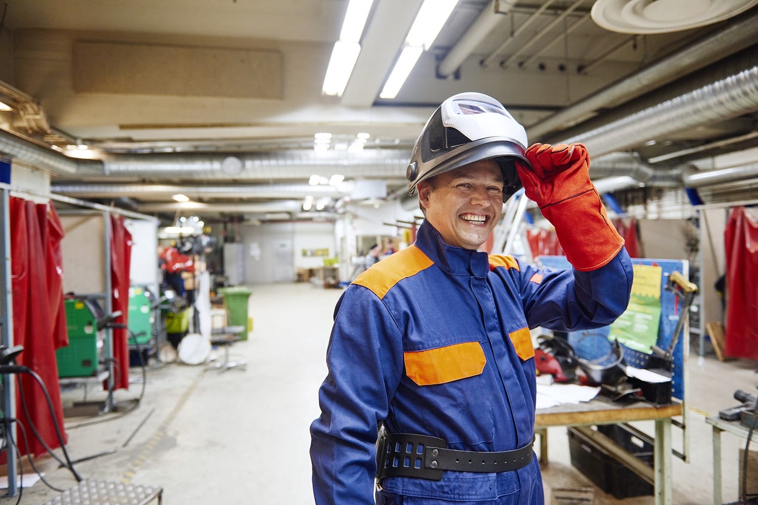 man lifting welders mask wearing overalls and smiling