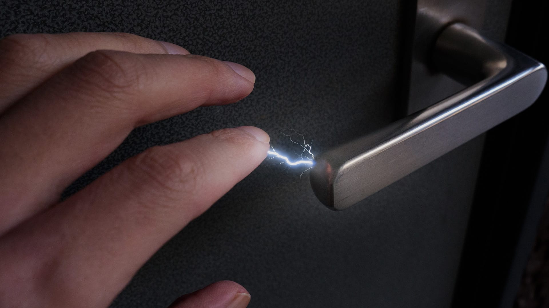 Static electricity spark between hand and metal door handle for anti-static and arc flash safety guide.