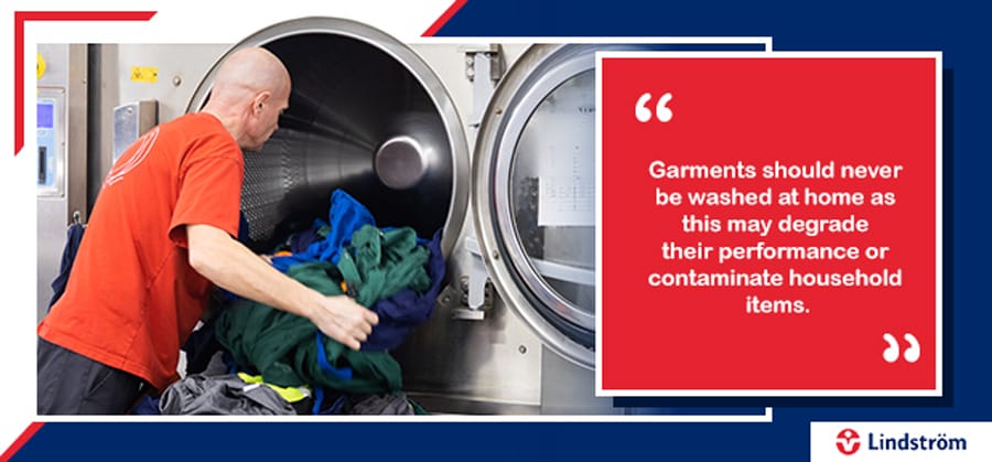 Worker loading PPE into industrial washing machine with garment care warning.