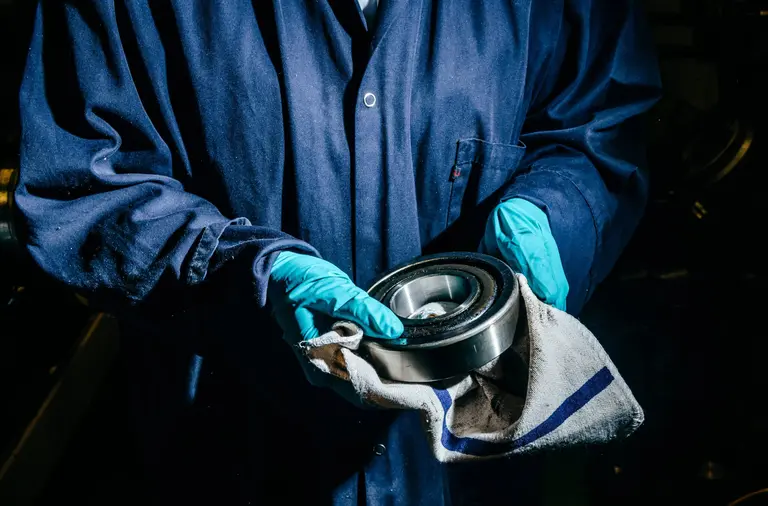 Darbuotojas su apsauginėmis pirštinėmis valo metalinę detalę daugkartine Lindström pramonine šluoste