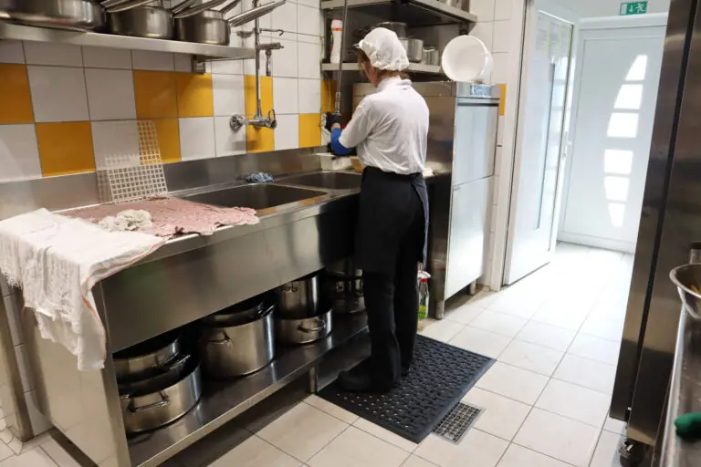 Zamestnankyňa stojí na protiúnavovej protišmykovej rohoži pri umývacom centre v profesionálnej kuchyni.